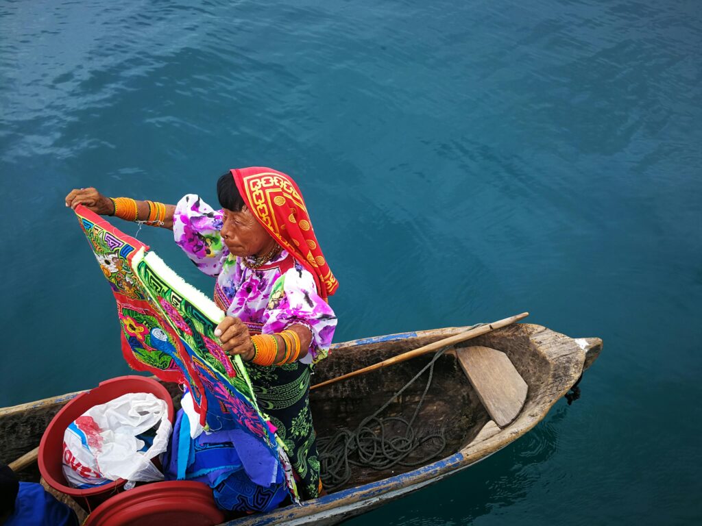 Guna Yala woman in a handcrafted canoe holding colorful textiles in Panama in the San Blas region.